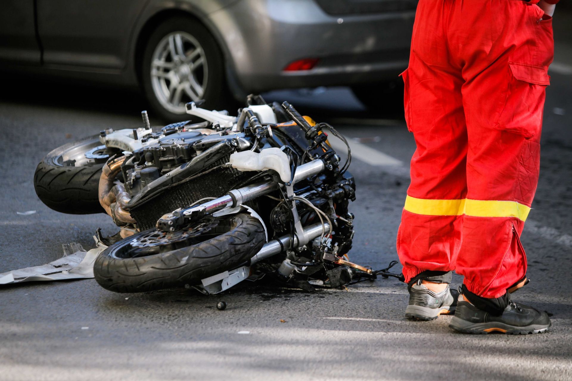 a man in red overalls is standing next to a motorcycle that has crashed into a car