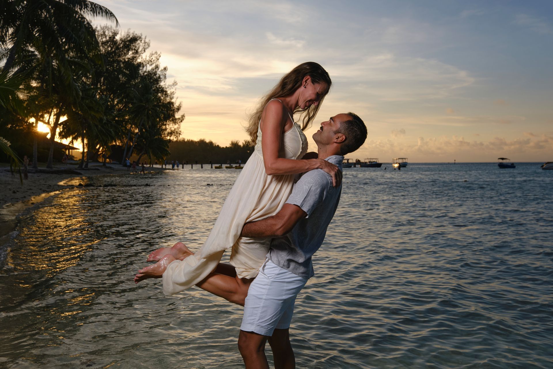 A man is holding a woman in his arms on the beach at sunset.
