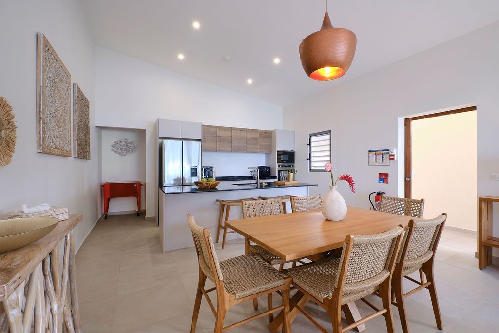 A dining room with a table and chairs and a kitchen in the background.