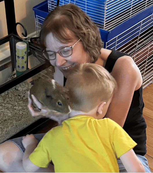 Woman and child holding a guinea pig, smiling, indoors near a cage.