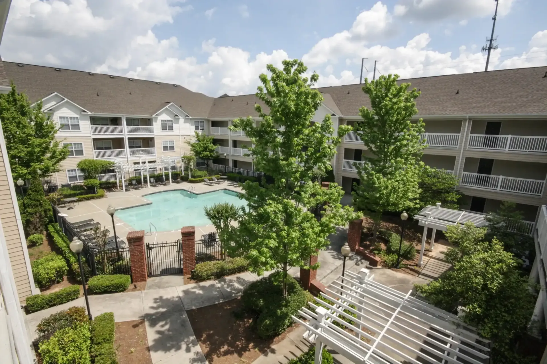 A high-angle view of an apartment complex courtyard featuring a swimming pool, surrounding trees, and a wooden pergola.