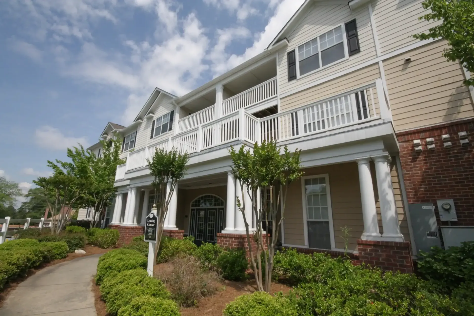 Ranch-style house with brick and gray exterior, pillars, surrounded by greenery and lawn.