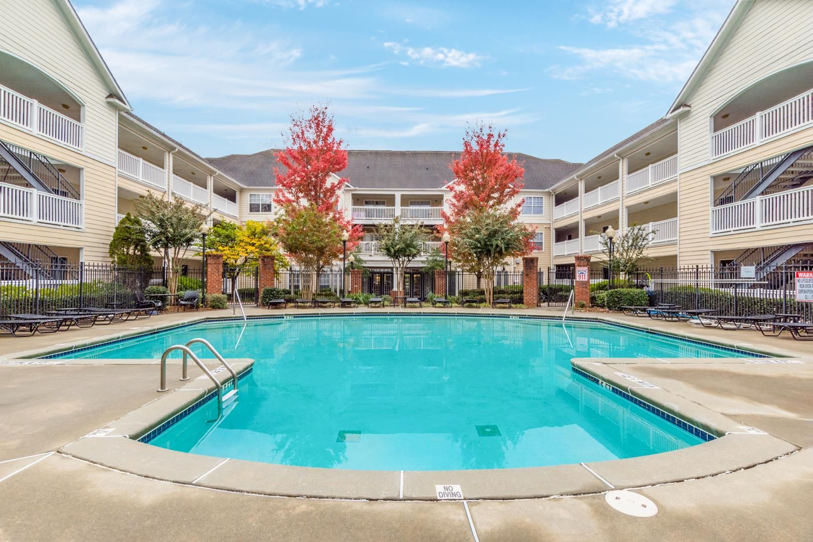 A rectangular swimming pool surrounded by a concrete deck between two multi-story apartment buildings with balconies.