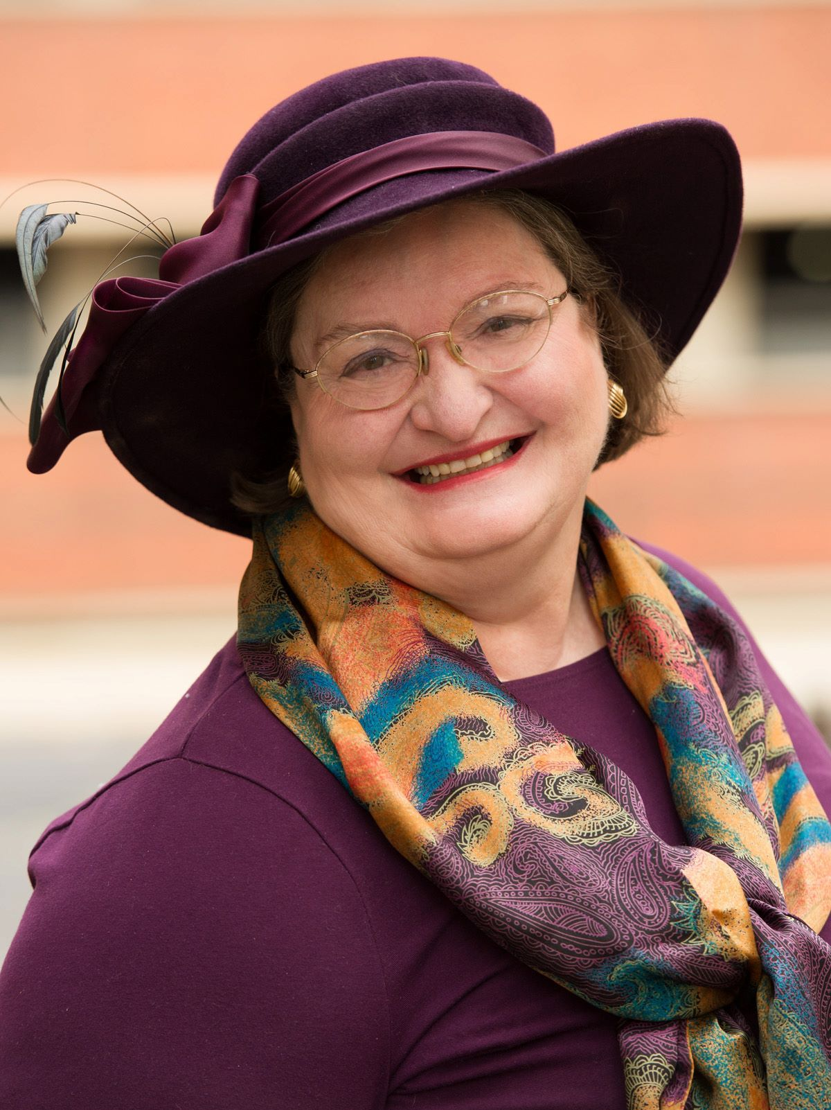 Woman smiling, wearing purple hat, scarf, glasses, and top.
