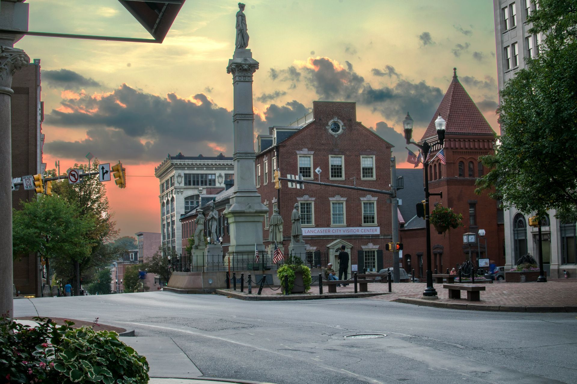 Town square with monument at dusk. Buildings, street, and colorful sky.