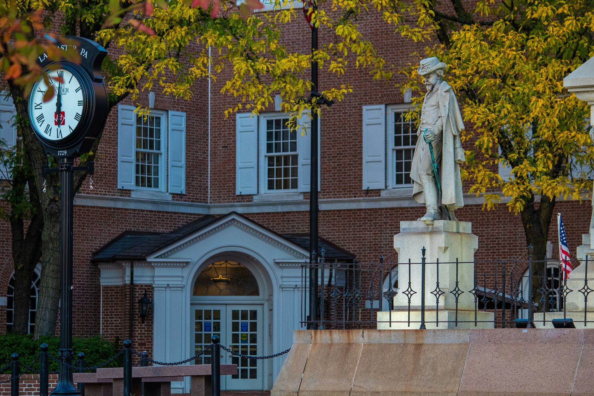 Clock, statue, and building with white shutters; autumn foliage.