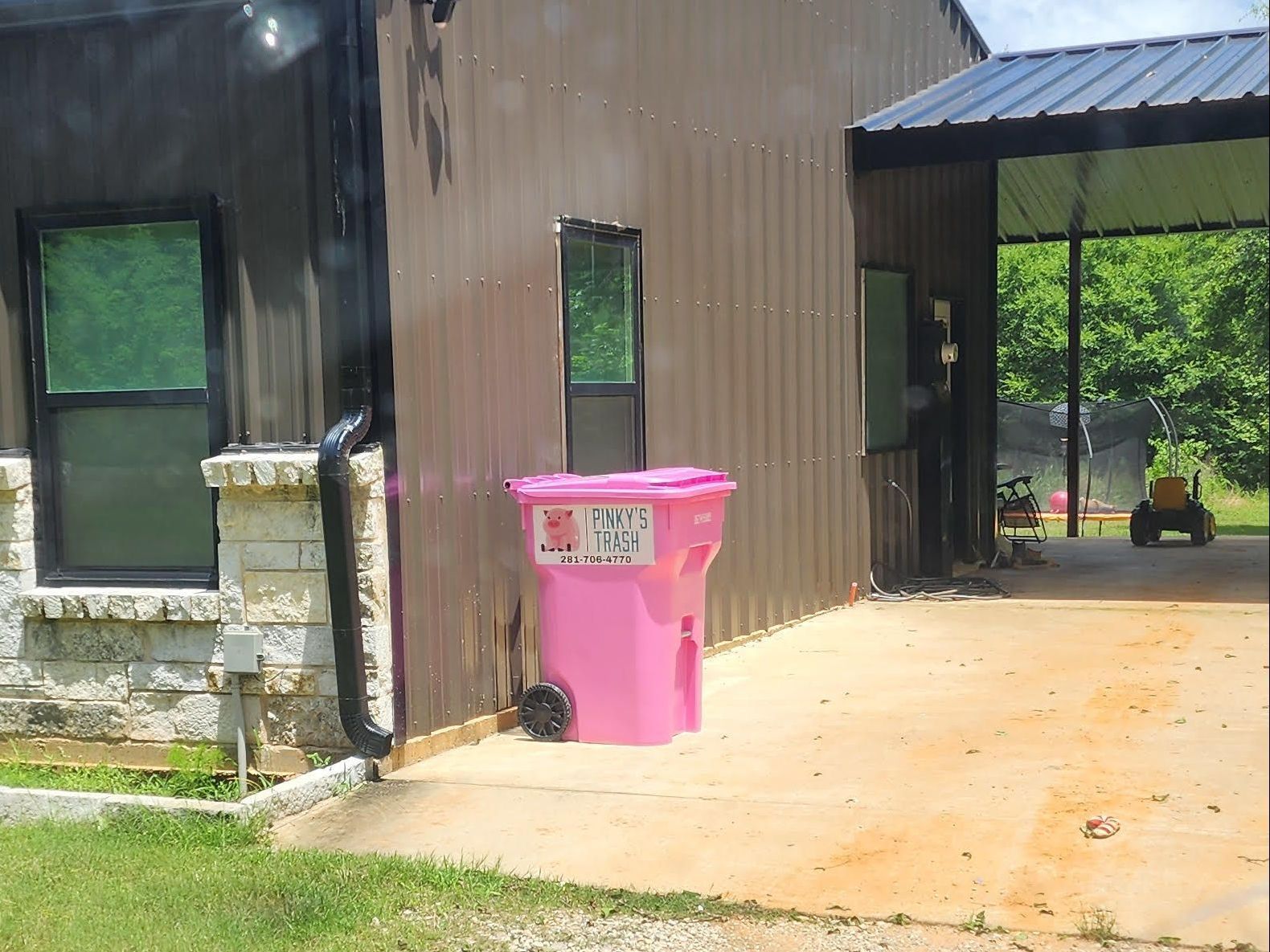 A pink trash can is sitting in front of a house.