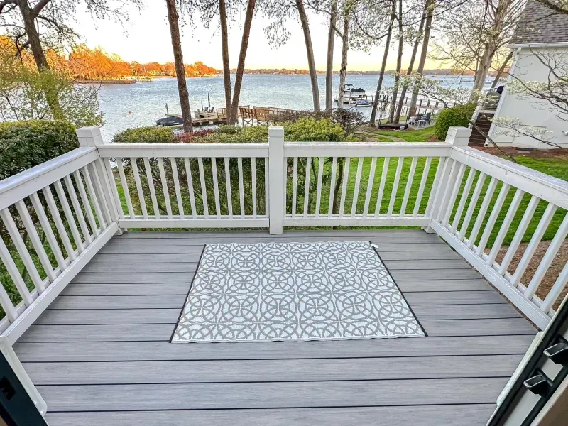 A deck with a white railing and a rug on it overlooking a lake.