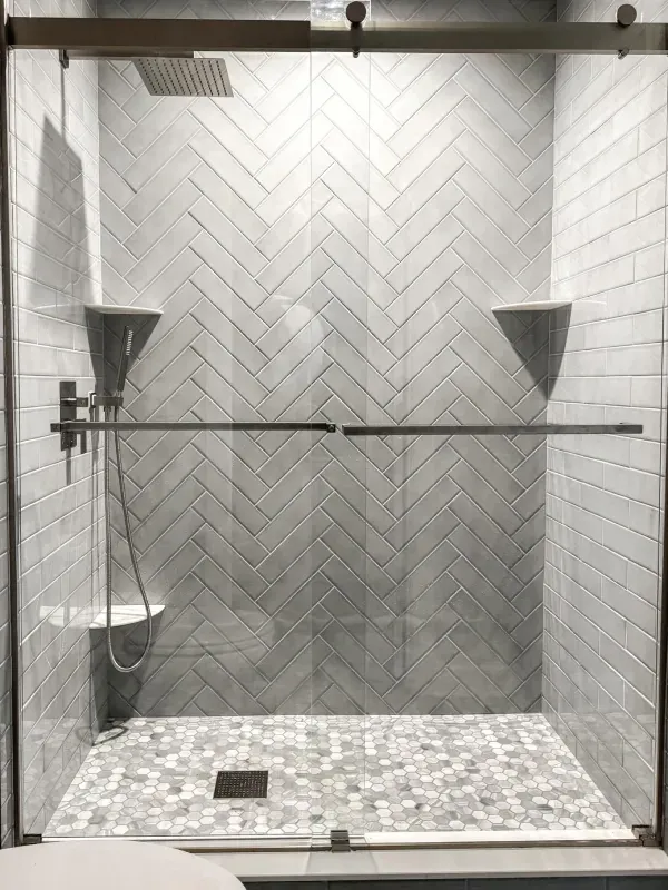 A black and white photo of a shower with a sliding glass door.