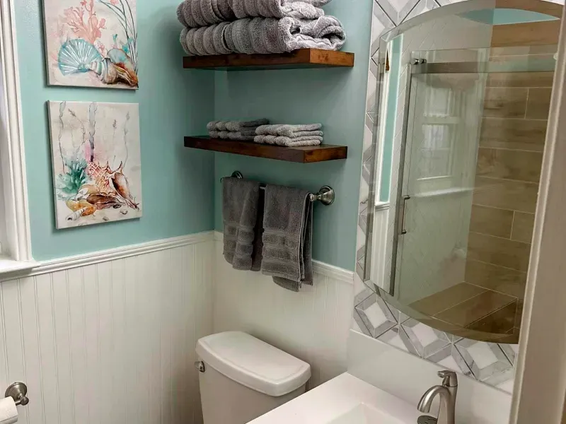 A bathroom with a toilet , sink , mirror and shelves.