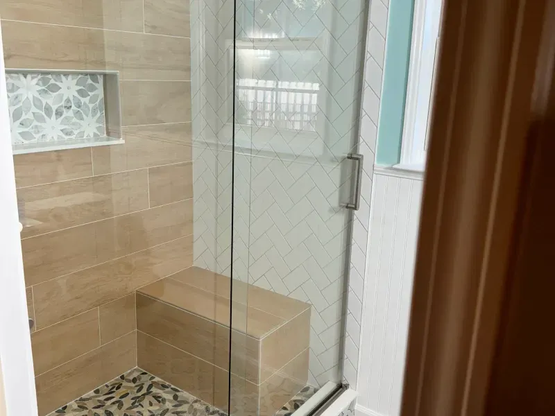A bathroom with a glass shower door and a bench.