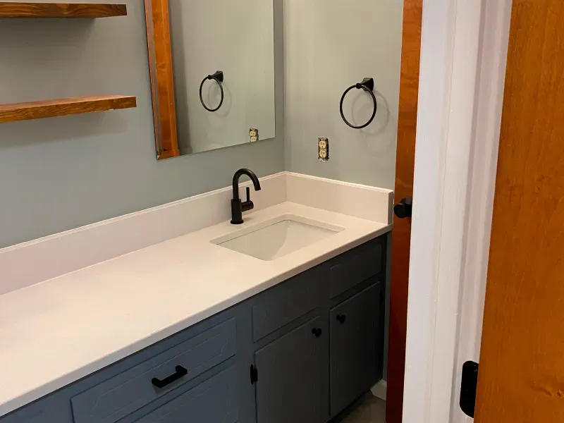 A bathroom with blue cabinets , a sink and a mirror.