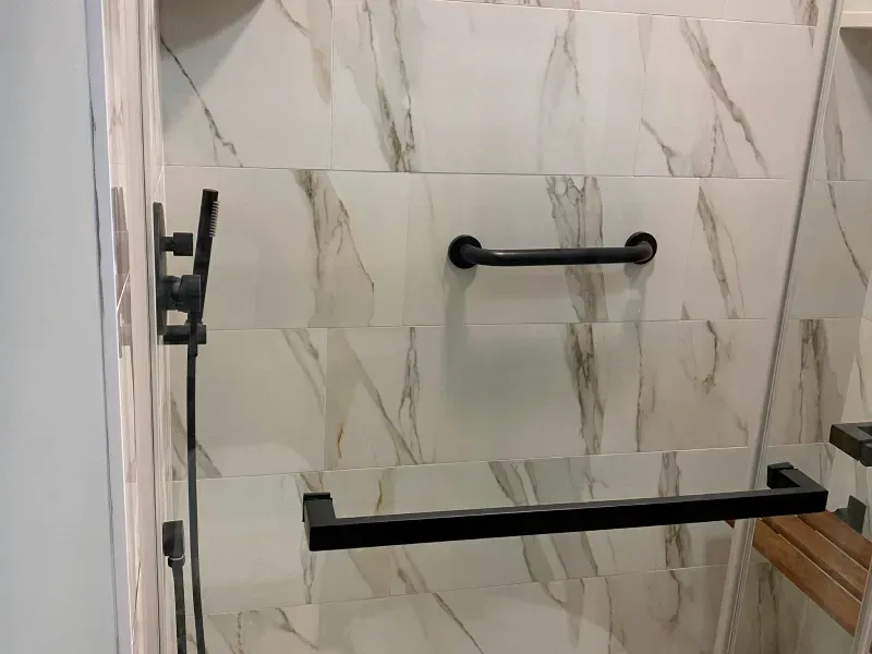 A bathroom with marble tiles and a black handle on the shower door.