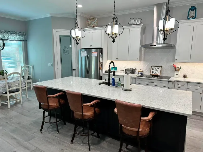 A kitchen with a large island , stools , and a refrigerator.