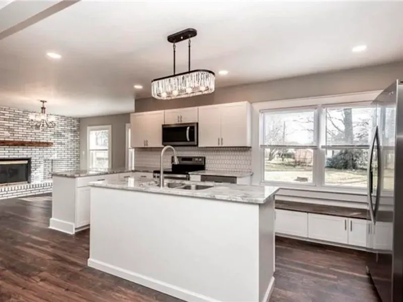 A kitchen with white cabinets , stainless steel appliances , a large island and a fireplace.