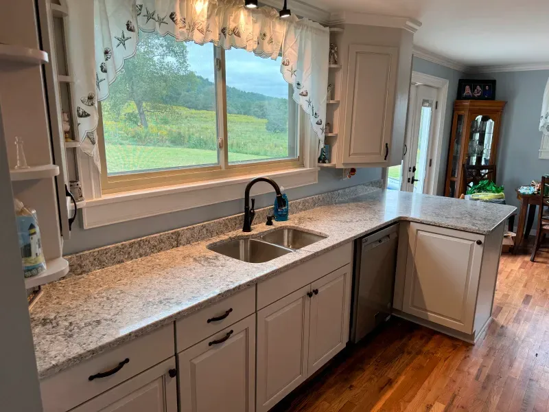 A kitchen with white cabinets , granite counter tops , a sink and a window.