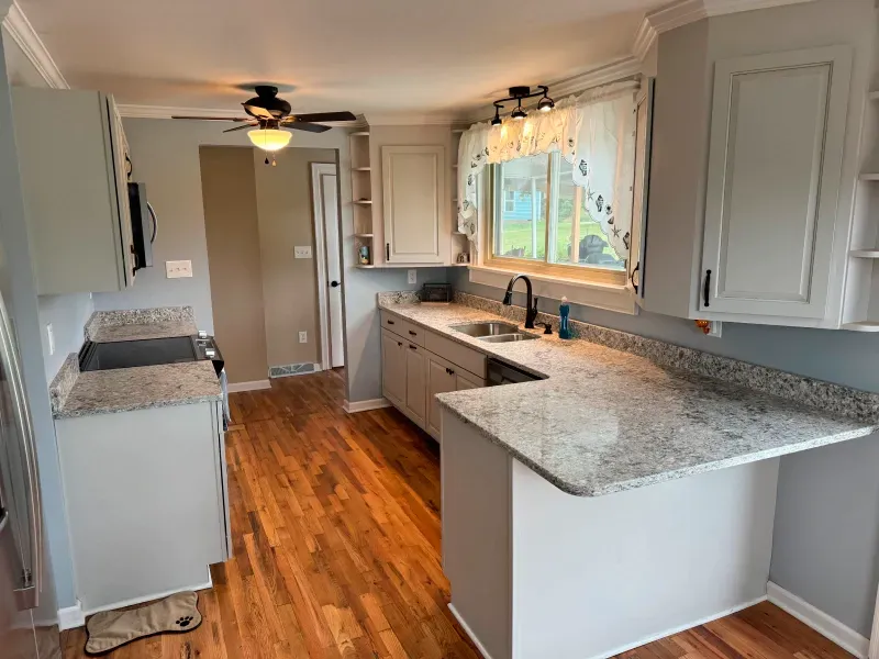 A kitchen with granite counter tops , white cabinets and hardwood floors.