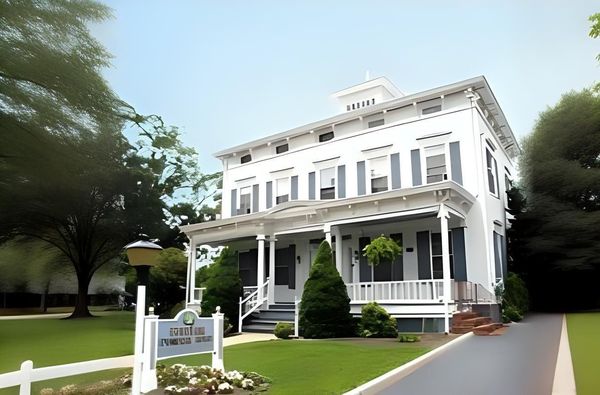 White Victorian house with gray shutters, porch, and a sign on the lawn.