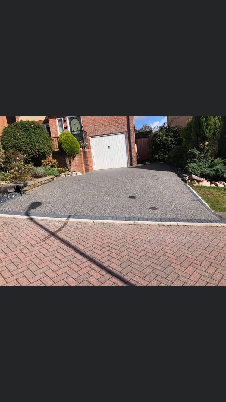 Grey resin driveway leading up to a white garage, bordered by block paving.