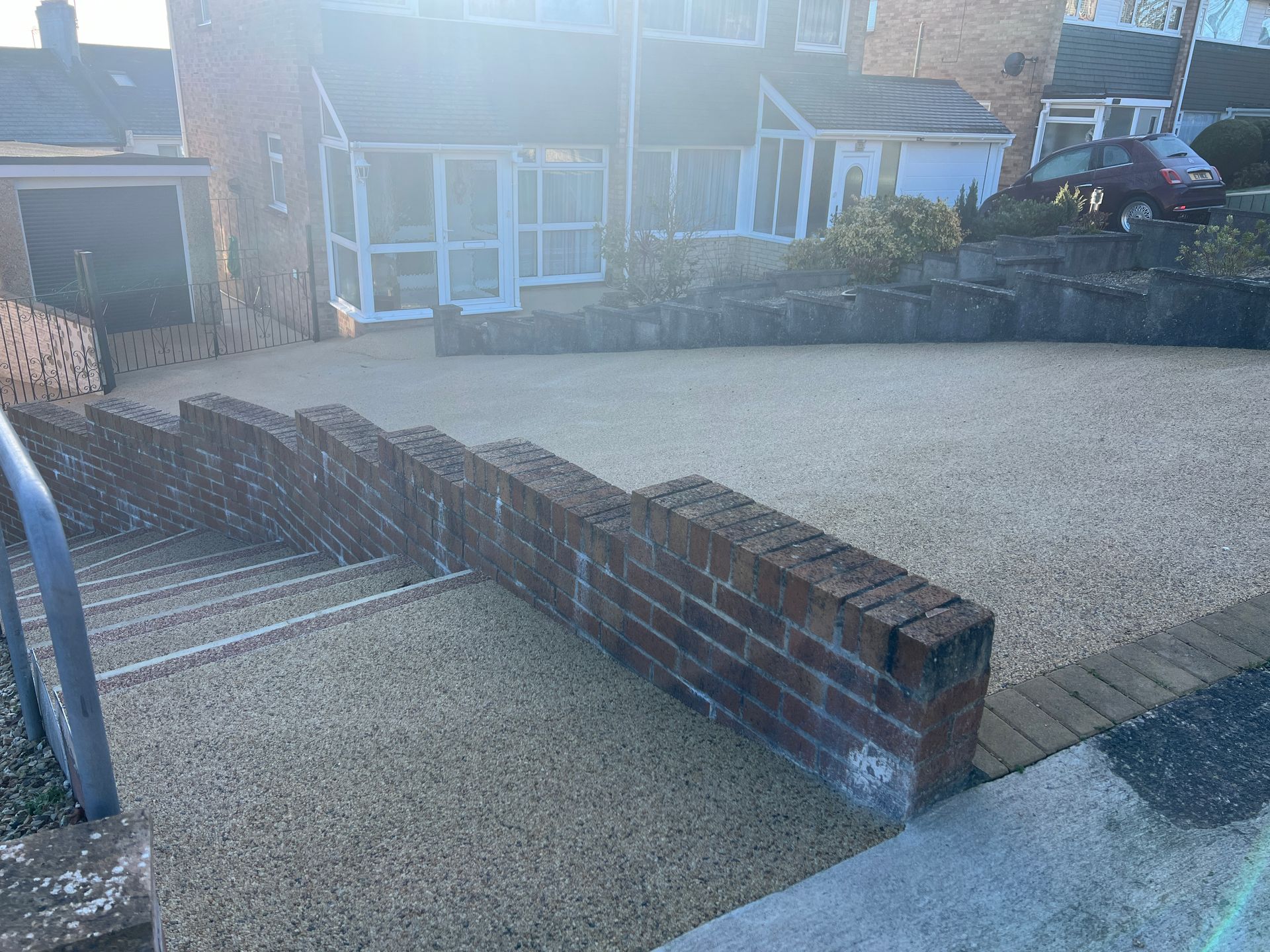 Brand-new resin driveway next to resin surfaced steps installed outside a brick house.