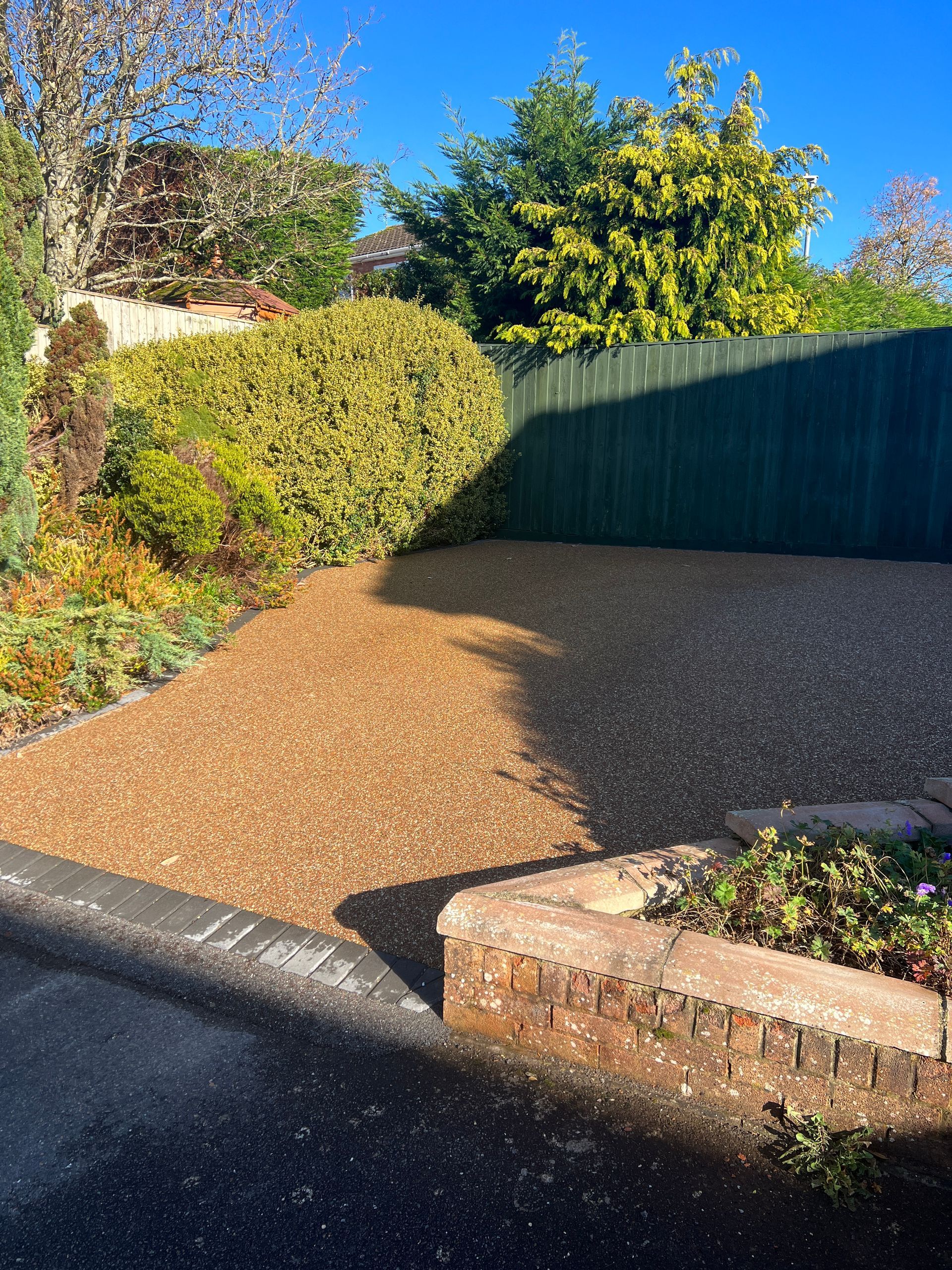 Brown resin driveway with grey border, surrounded by green bushes.