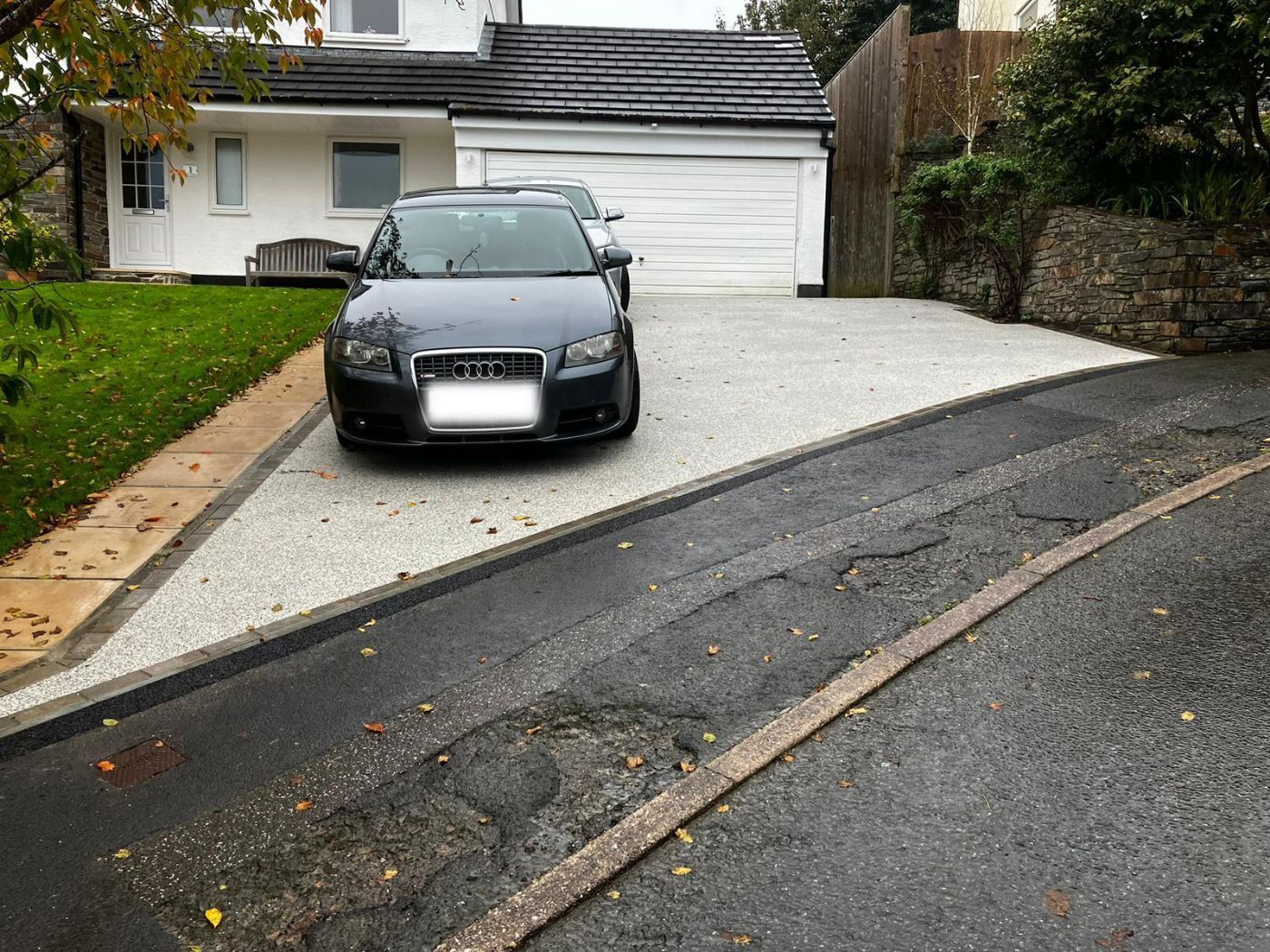 Light grey resin driveway with a black car parked on it, in front of a white bungalow.
