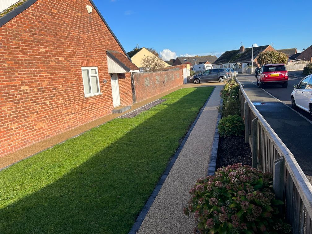 A resin pathway in gold with grass on one side of it, and a flower bed on the other.