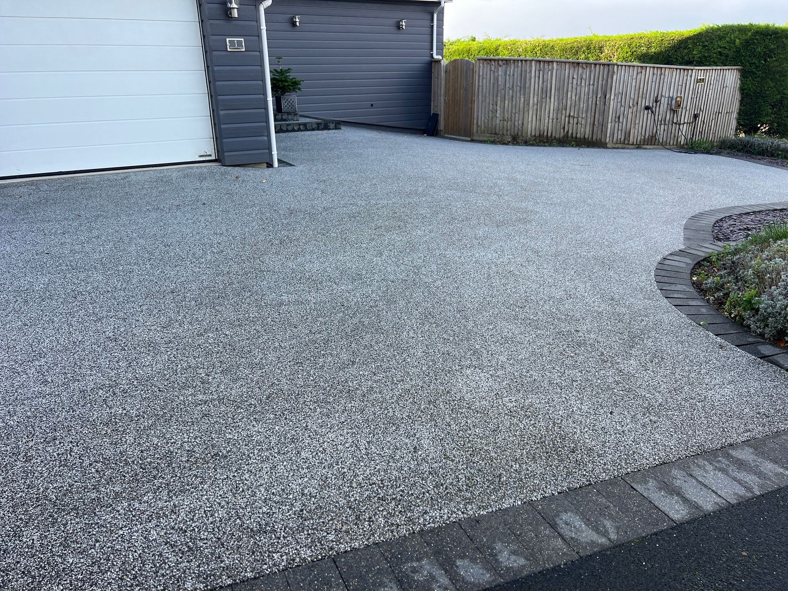 Grey resin driveway, with grey block paving outside a grey home with a garage.