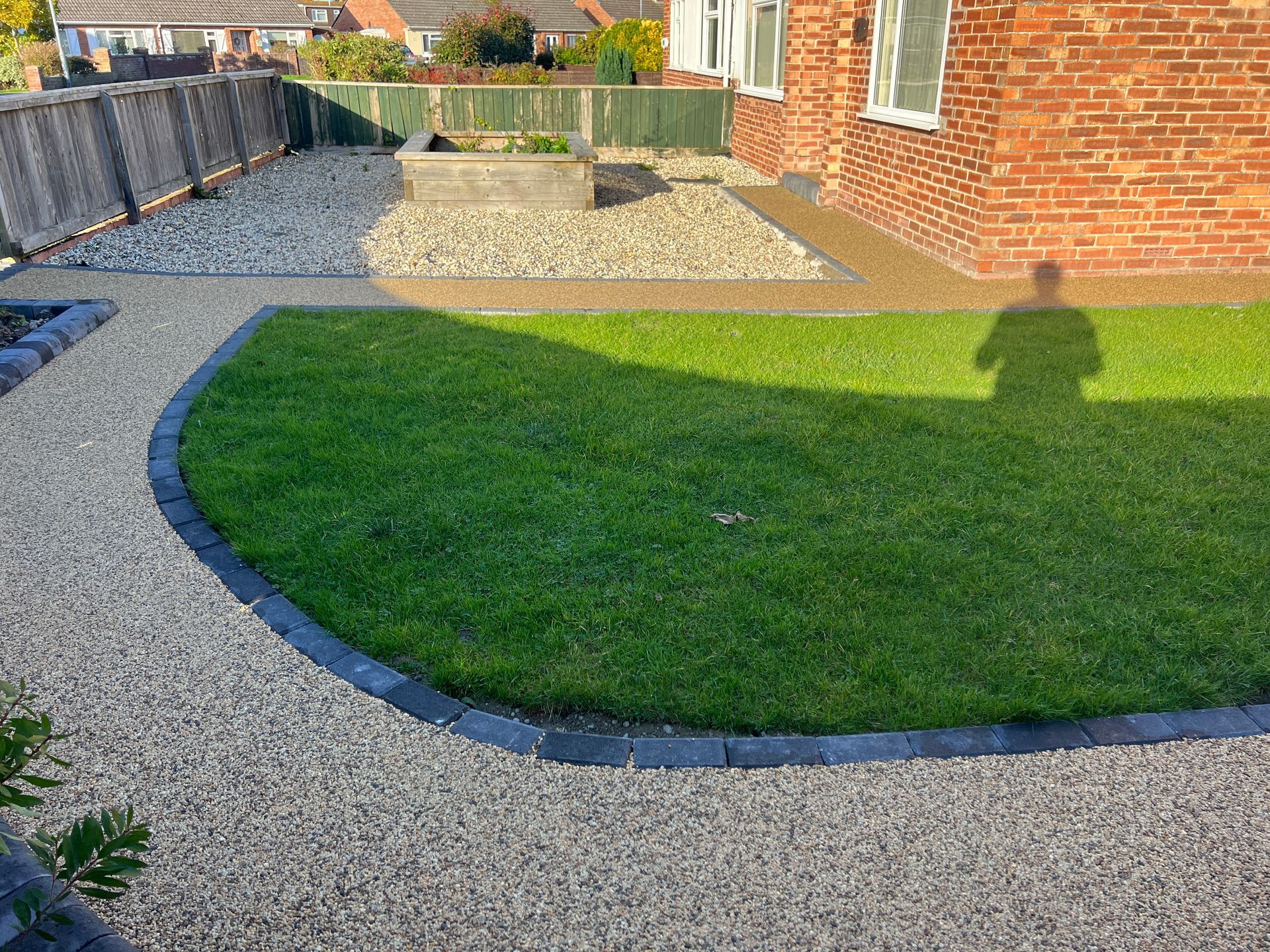 Sand coloured resin path and driveway surrounding by grass plots outside a red brick house.