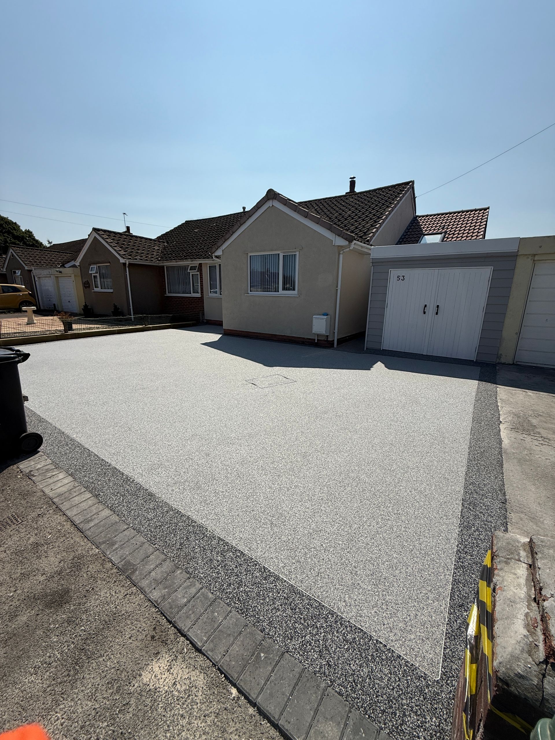 A gravel driveway in front of a bungalow with a garage. The sky is blue.