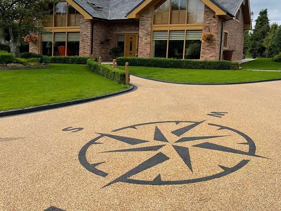 A beige resin driveway with a black resin compass on it, outside a large brick building.