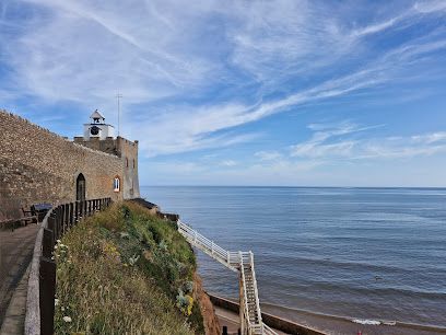 Coastal view: stone castle, ocean, blue sky with wispy clouds, white stairs leading to beach.
