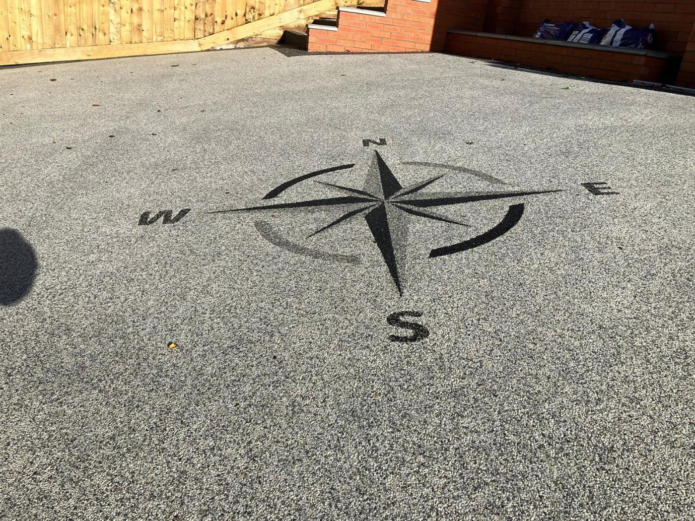 A grey resin driveway and patio with a black and dark grey compass shape at the entrance.
