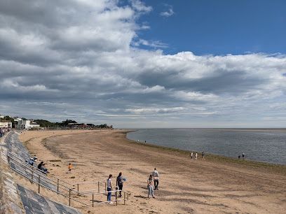 Beach with people, ocean under cloudy sky.