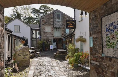 Stone courtyard with buildings, sign for Dartmoor Gin, and cobbled path.