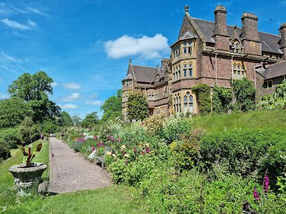 A large brick building with multiple turrets overlooks a garden path filled with flowers under a blue sky.