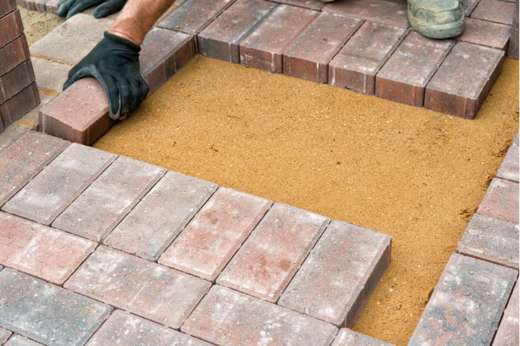 Red and brown block pavers for a driveway, with visible sand underneath them.