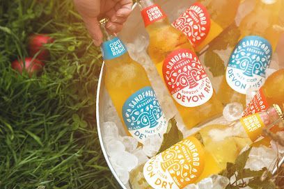 Hand holding a bottle of Sandford Orchards cider in an ice bucket with other bottles, grass, and apples.