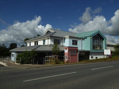 A two-story building with a teal and blue facade, beside a road, under a cloudy sky.