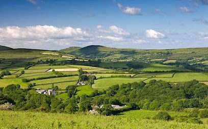 Green fields, trees, and rolling hills under a blue sky with fluffy clouds.