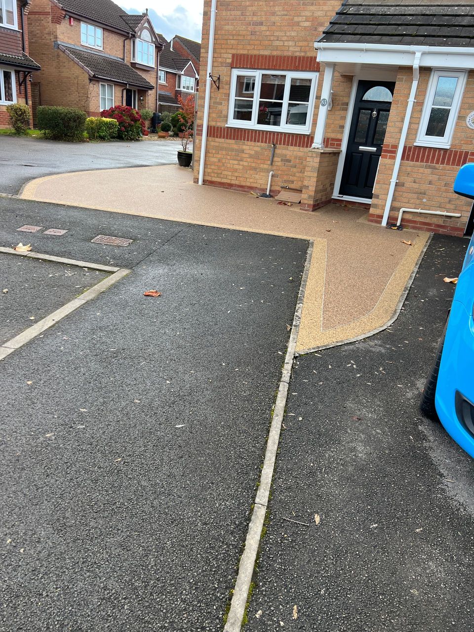 A 10-year-old resin driveway installation in a brown colour, with a purple flower bed on the right-hand side of the driveway.