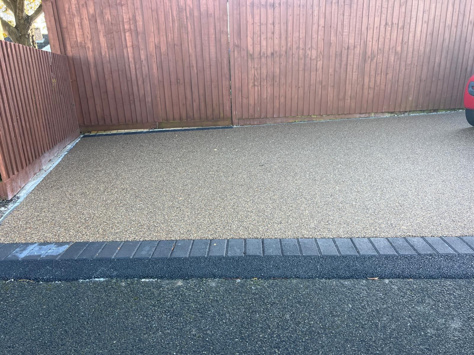 A car is parked in a driveway next to a wooden fence.