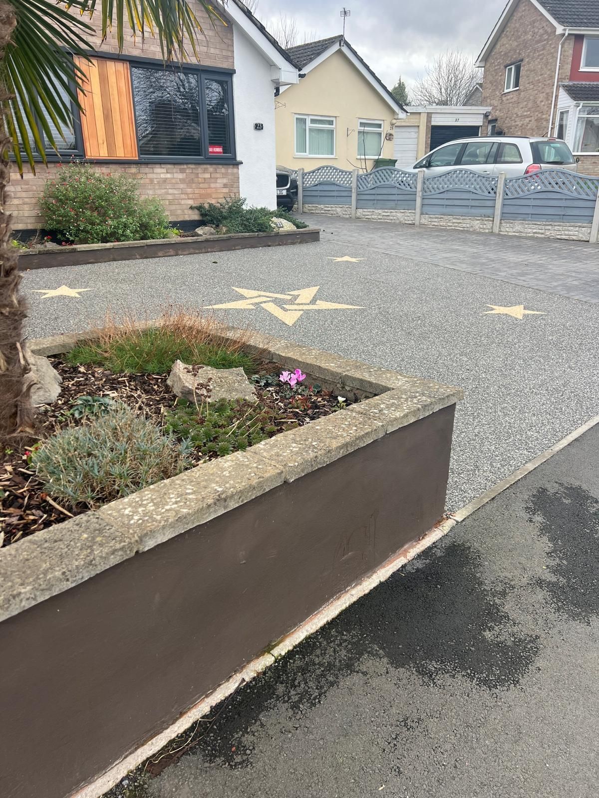 A driveway with a planter in the middle of it and a house in the background.