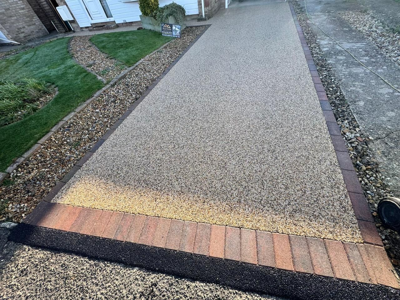 A gravel driveway bordered by brick and a strip of grass.