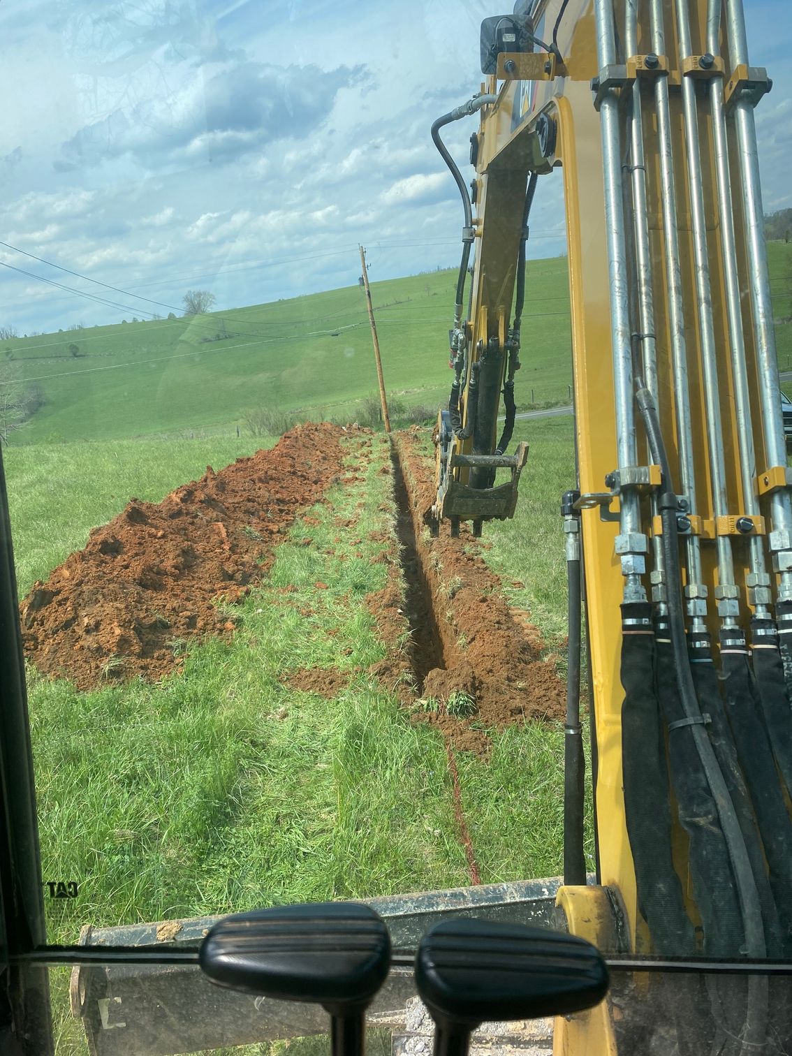 A yellow excavator is digging a trench in a grassy field.