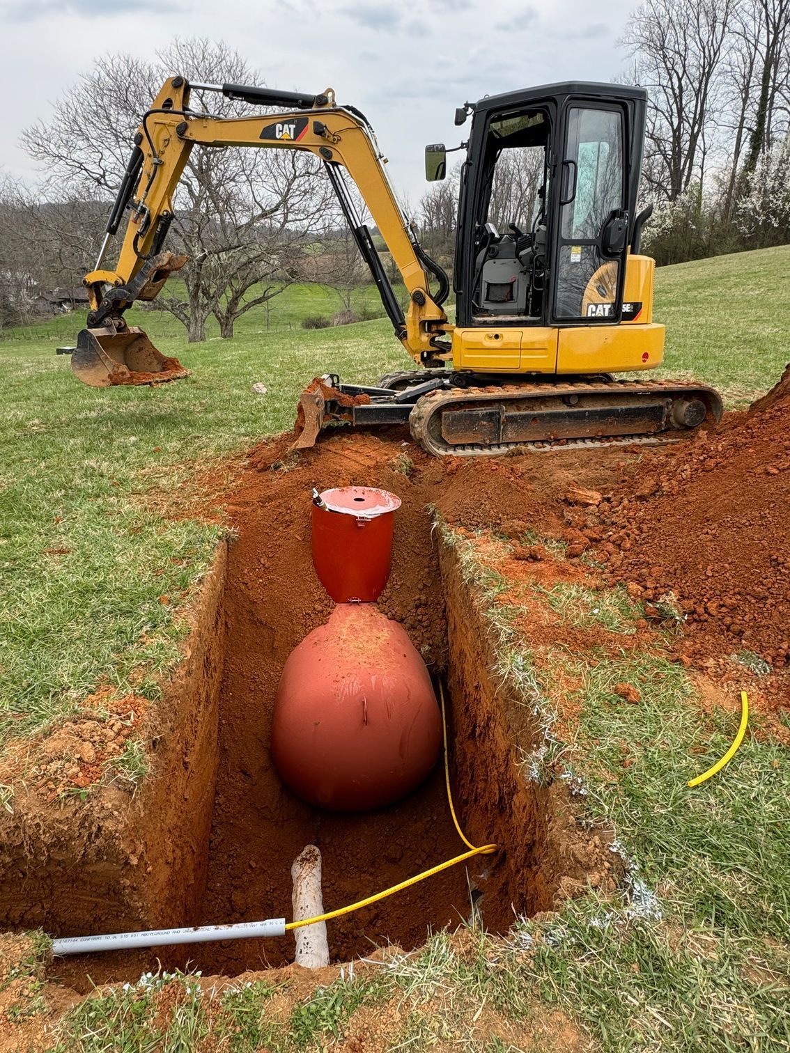 A yellow excavator is digging a hole in the ground next to a large red ball.