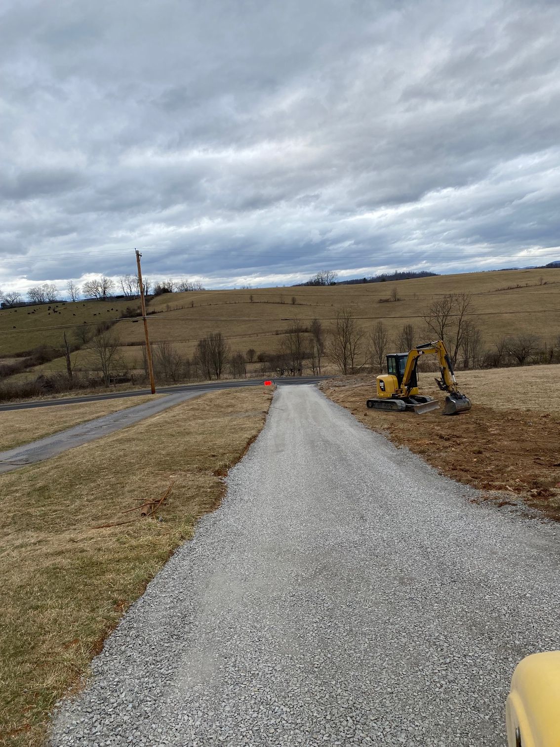 A gravel road with a yellow excavator on the side of it.