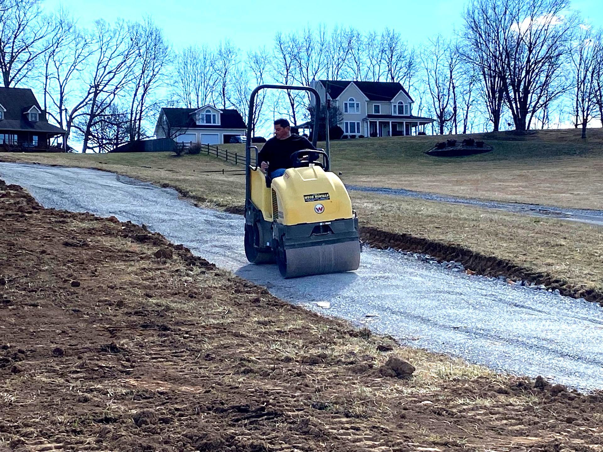 A man is driving a roller down a dirt road.