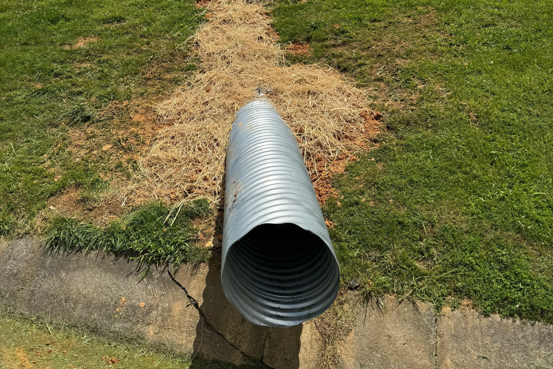 A large metal pipe is sitting in the middle of a grassy field.