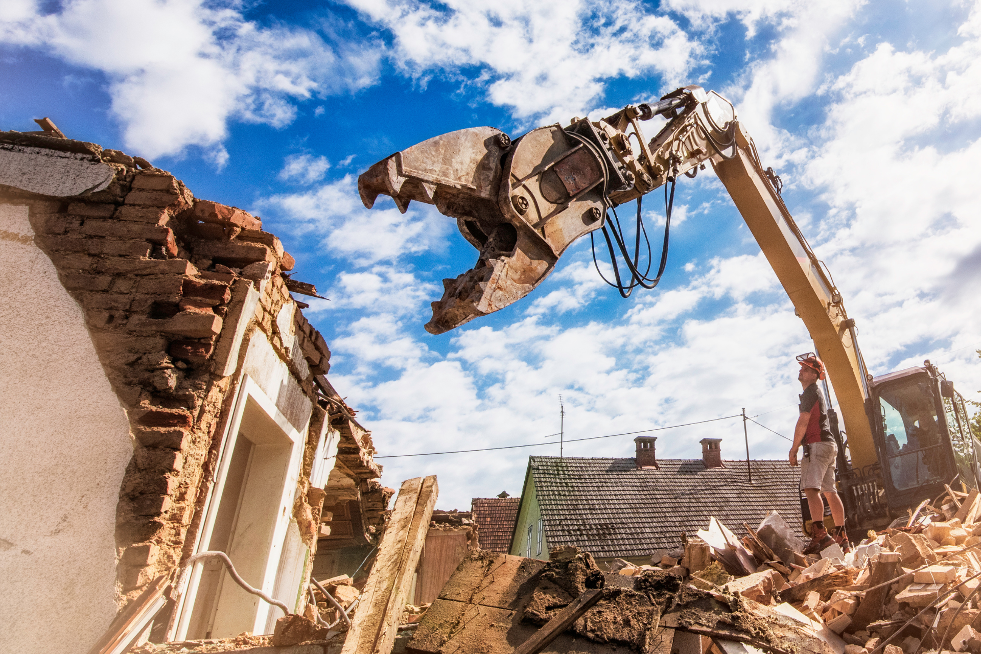 A large excavator is demolishing a building with a blue sky in the background.